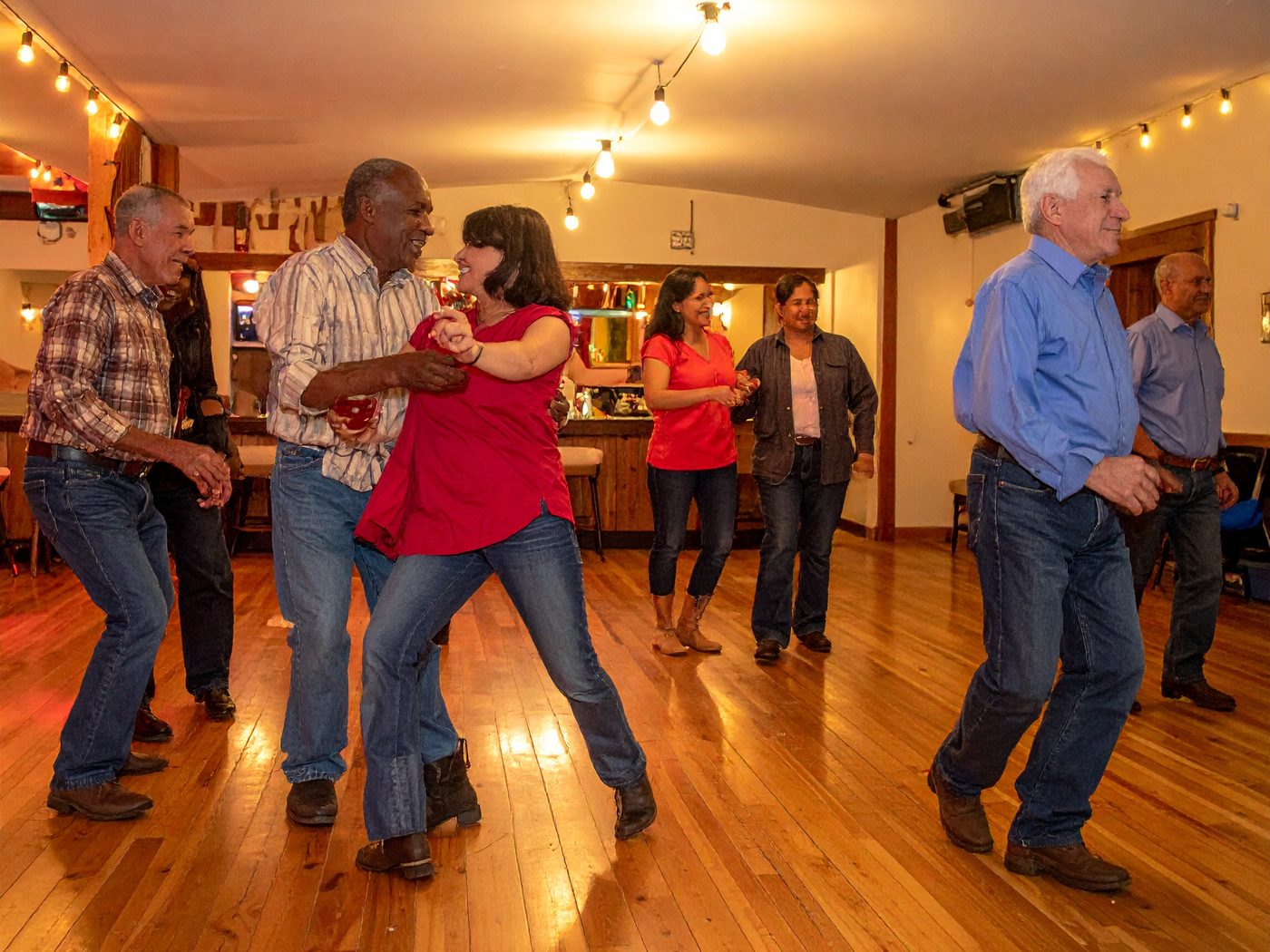 Illustration of smiling dancers in jeans and western shirts dancing a country two-step on a wood floor